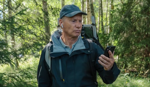 En man som står i skogen och tittar på sin mobiltelefon.